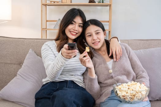 Two young women watching TV and eating popcorn on couch. Concept of relaxation and friendship.