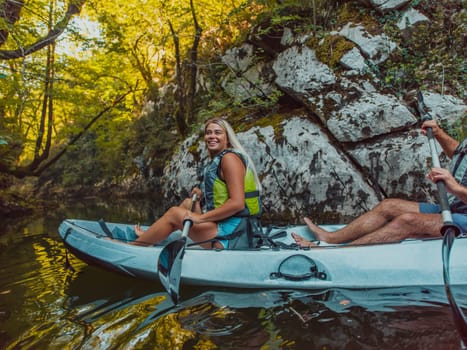 A young couple enjoying an idyllic kayak ride in the middle of a beautiful river surrounded by forest greenery.