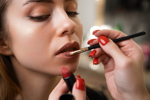 A makeup artist gently applies lipstick with a special brush