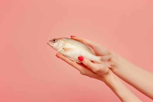 Woman's hand holding a fish on pink background with red manicure beauty and nature connection concept in fashion photography