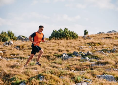 A muscular male athlete runs along a rugged mountain path at sunrise, surrounded by breathtaking rocky landscapes and natural beauty.