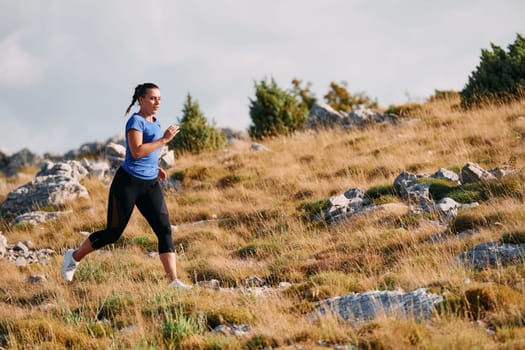 A determined female athlete runs through a forest trail at sunrise, surrounded by breathtaking natural beauty and vibrant greenery.