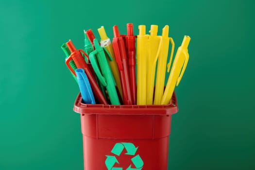 Recycling bin filled with colored pencils on green background for art supplies and education concept