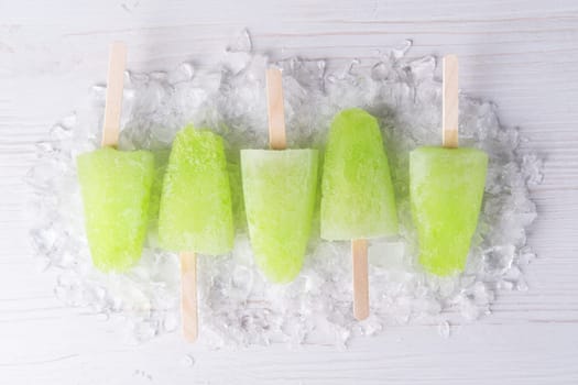 Homemade popsicles with lime juice and mint, mojito fruit ice on a white wooden table.