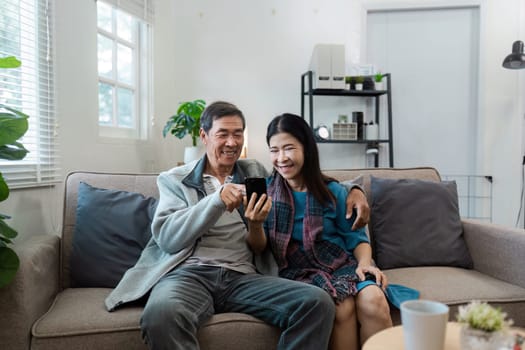 A man and woman are sitting on a couch, both looking at a cell phone. They seem to be enjoying their time together