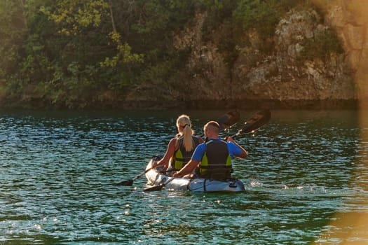 A young couple enjoying an idyllic kayak ride in the middle of a beautiful river surrounded by forest greenery in sunset time.