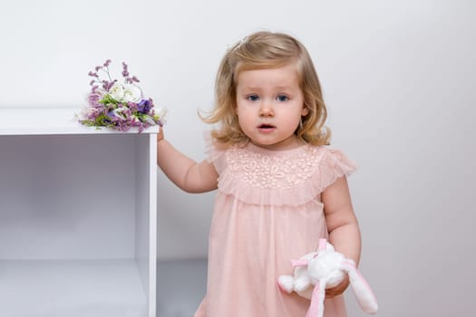 A two-year-old girl with the blue eyes in a pink tulle dress in a children's room