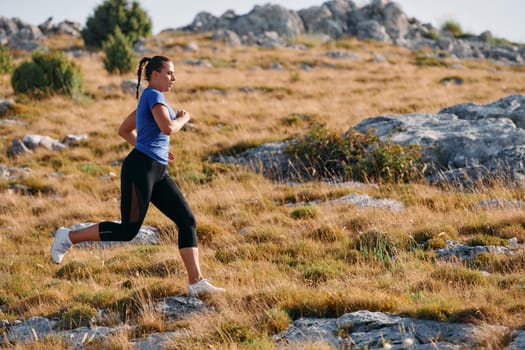 A determined female athlete runs through a forest trail at sunrise, surrounded by breathtaking natural beauty and vibrant greenery.