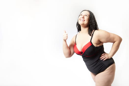 Portrait of attractive dreamy thick woman in red black swimsuit posing on white background. Body positive, photoshoot, selfie. Funny plus size model