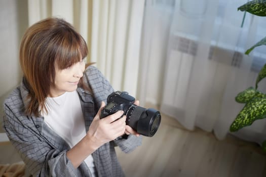 Senior old elderly woman with black camera with a large lens indoors in the studio. Professional photographer. Age Hobby