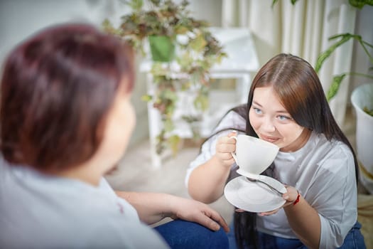 Happy Overweight family with mother and daughter drinking tea or coffee in room. Middle aged woman and teenager girl having fun and joy