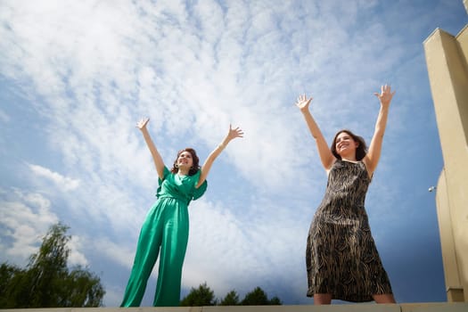 Happy Girls Enjoying Summer Day Together in the Park. Two young women stand on a platform in a park under a bright summer sky, smiling and relaxed