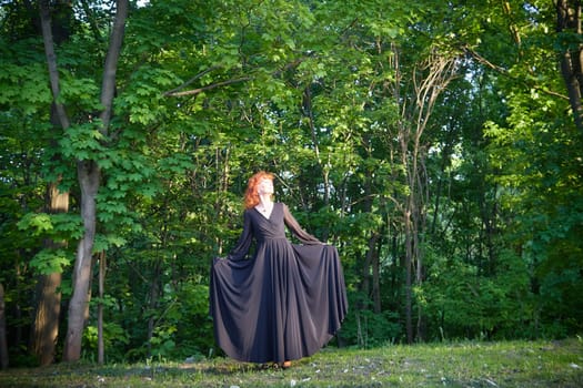 Elegant senior mature Woman dancing in Black Dress in green park. Woman with red hair posing on nature