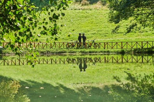 A blissful couple, adorned in professional cycling gear, enjoys a romantic bicycle ride through a park, surrounded by modern natural attractions, radiating love and happiness.