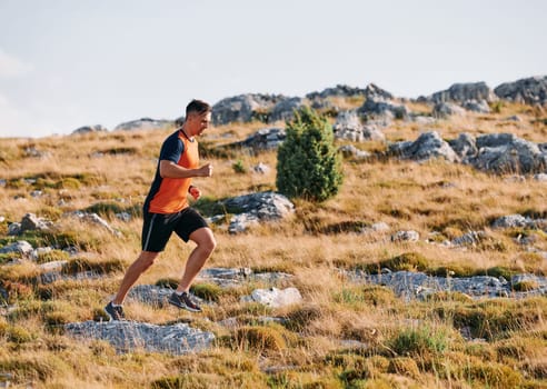 A muscular male athlete runs along a rugged mountain path at sunrise, surrounded by breathtaking rocky landscapes and natural beauty.