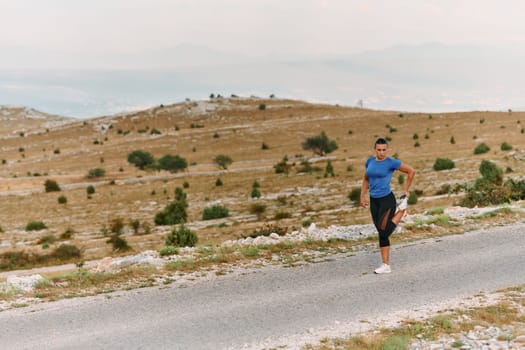 A determined female athlete stretches her muscles after a strenuous run through rugged mountain terrain, surrounded by breathtaking rocky landscapes.