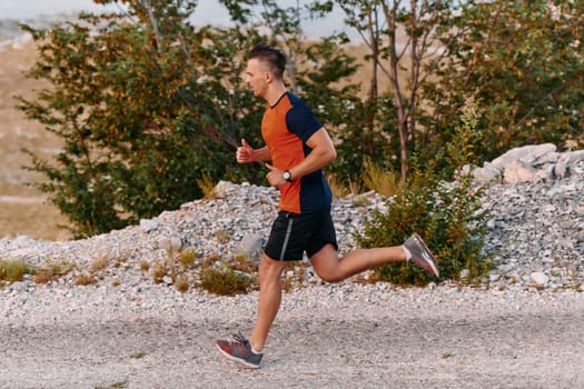 A muscular male athlete runs along a rugged mountain path at sunrise, surrounded by breathtaking rocky landscapes and natural beauty.