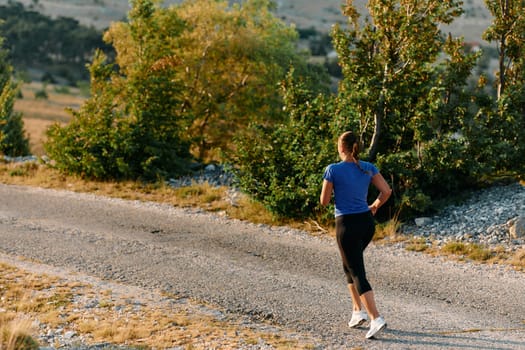 A determined female athlete runs through a forest trail at sunrise, surrounded by breathtaking natural beauty and vibrant greenery.