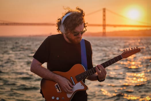 Hipster street musician in black playing electric guitar in street outdoors on sunset