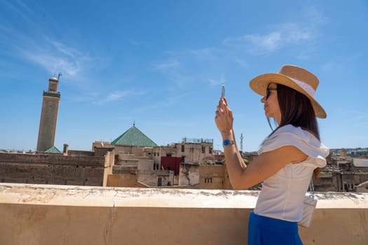 Young Woman in Hat Photographing Fez Cityscape with Smartphone, Morocco
