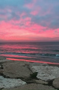 The image shows a beautiful sunset over the ocean, with rocks in the foreground. The sky is filled with colorful clouds, creating a serene afterglow over the fluid water