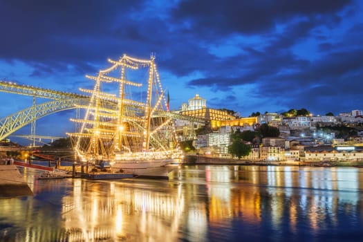 View of Vila Nova de Gaia city with a sailing ship and Dom Luis I bridge over Douro river in the evening. Porto, Portugal