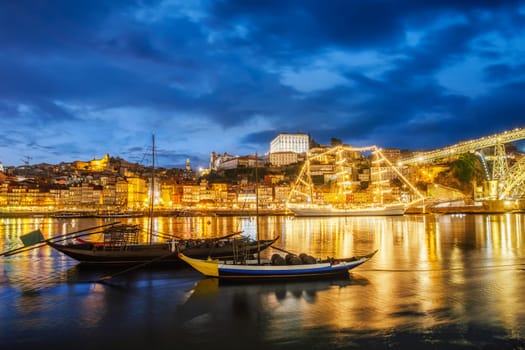 View of Porto city and Douro river with traditional boats with port wine barrels and sailing ship from famous tourist viewpoint Marginal de Gaia riverfront in night. Porto, Vila Nova de Gaia, Portugal