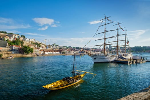 View of Vila Nova de Gaia city with sailing ship and traditional boat with port wine barrels and Douro river with tourist boats on sunset. Porto, , Portugal