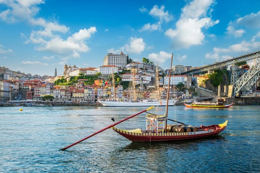 View of Porto city and Douro river with traditional boats with port wine barrels and sailing ship from famous tourist viewpoint Marginal de Gaia riverfront. Porto, Vila Nova de Gaia, Portugal