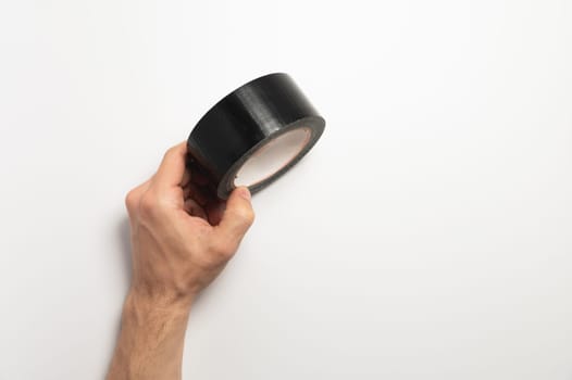 A roll of black reinforced adhesive tape, for sealing joints of roofing materials, when installing the roof, lying, on a white background in a man hand.