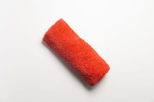 Fluffy orange-red rolled up towel on white background.