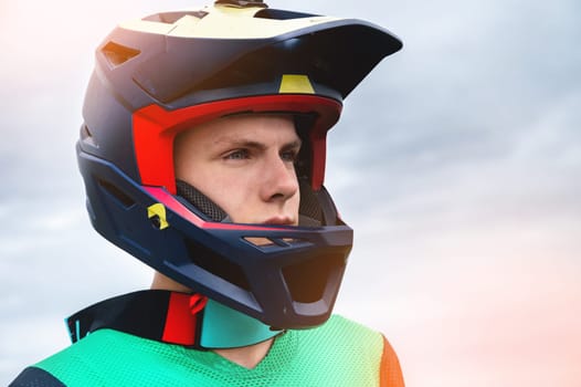 Close-up portrait of a confident handsome young athlete wearing a stylish helmet looking at the camera with eyes full of determination, ready to race on a summer day outdoors.