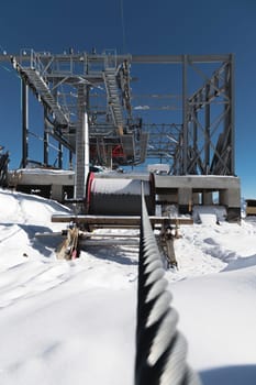 A cable car station under construction high in the mountains in winter. Focus on a close-up of a thick cable car cable covered with snow.