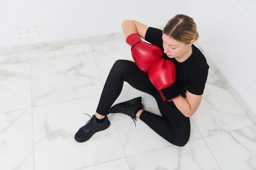 View from above of a confident young athlete woman posing in red boxing gloves, isolated over white background. Copy advertising space