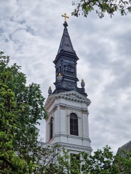 BUDAPEST, HUNGARY - 2023-05-06: Picture the majestic white dome of an church piercing the sky, framed by the vibrant green leaves of tall trees. The juxtaposition of earthly foliage and heavenly architecture creates a scene of profound spiritual harmony, inviting contemplation and awe.