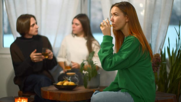 Students talk and relax in cozy cafe. Media. Beautiful young woman is drinking tea on background of talking couple. Students relax and drink tea in college cafe.