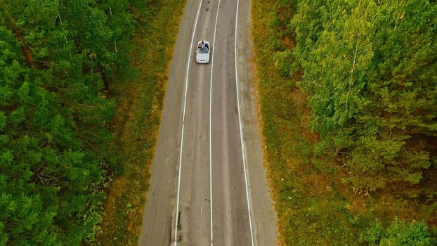 Aerial top view of white convertible car driving through empty rural road. Footage. Traveling at cabriolet on a summer day