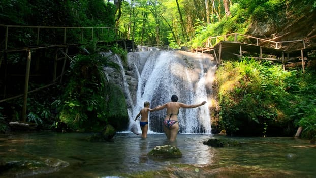 Woman and boy child bathing in beautiful waterfall in dense jungles. Creative. Woman and a boy in cold mountainous river