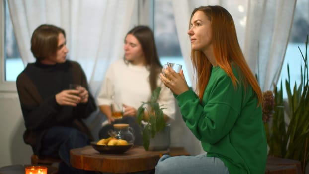 Students talk and relax in cozy cafe. Media. Beautiful young woman is drinking tea on background of talking couple. Students relax and drink tea in college cafe.