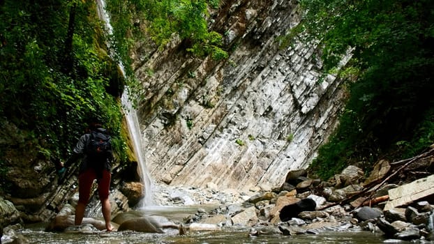 Beautiful waterfall in green forest. Creative. Woman crossing tropical river in mountain jungle