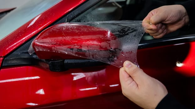 The master applies vinyl film to the side view mirror of a car