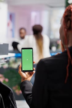 African american woman holding mobile phone with green screen while choosing clothes in boutique. Mall customer using smartphone with chroma key mock up for comparing prices online