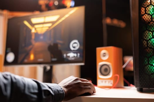 Man in living room playing video games on gaming PC at computer desk, enjoying day off, close up shot. Gamer using mouse to shoot enemies in online multiplayer game from neon lights ornate home