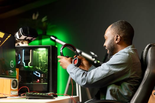 African american man putting headphones on while playing videogames at home to better immerse himself. Player participating in online multiplayer esports tournament, fighting to defeat enemies