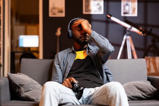 Man putting palm on forehead, feeling headache coming after receiving game over while playing videogames on gaming console. Gamer on couch getting high tension after being defeated