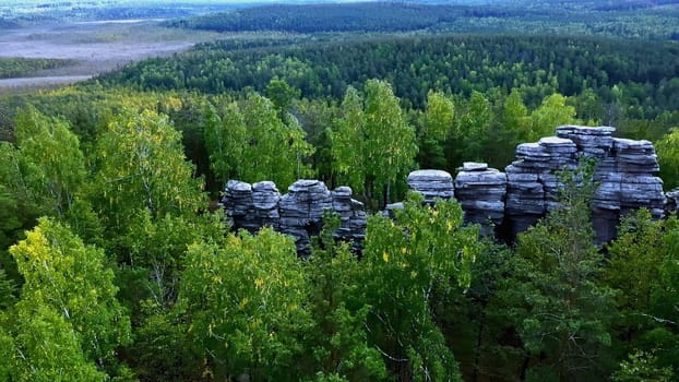 Aerial view of rock cliffs among green summer trees. Footage. Tops of the mountain cliffs in green forest