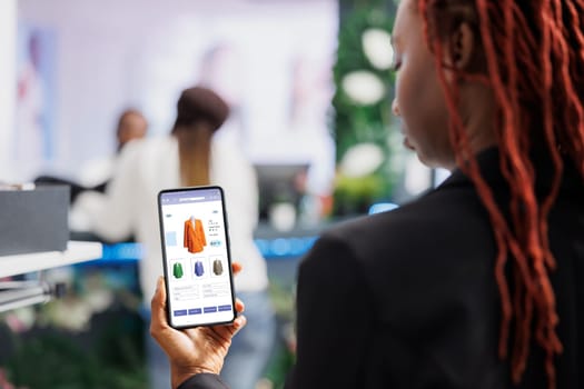 Customer looking at online clothing app shop, buying clothes on website while she sits in fashion boutique at mall. Buyer shopping online on digital store, retail merchandise items.