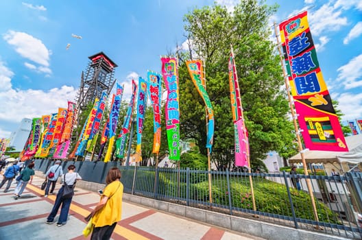 tokyo, ryogoku - may 17 2024: Japanese spectators walking along vibrant Japanese sumo nobori flags lining the path leading to the historic yagura-daiko tower of the Ryōgoku Kokugikan Sumo Stadium.