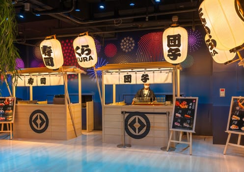 tokyo, ginza - may 14 2024: Japanese Kura Revolving Sushi Bar illuminated with fireworks decorations and paper lanterns used at matsuri summer festival, a chef cooking dango skewers at yatai counter.