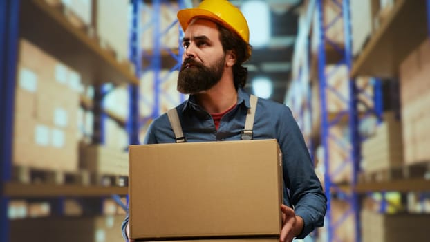 Packaging operator carrying stock boxes in warehouse, trying to organize merchandise on pallets. Employee maintaining inventory in industrial storage room, load and unload production.